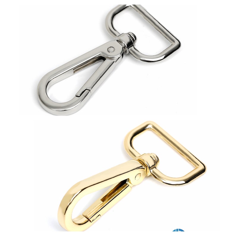 May include: Two metal swivel clasps. One is silver-colored, and the other is gold-colored. Each clasp has a spring-loaded hook and a rectangular D-ring. These clasps are likely used for attaching straps to bags or other accessories.