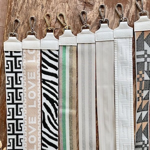 May include: Eight different white and black patterned straps with gold clasps. The straps are made of woven fabric and have a variety of patterns, including geometric, zebra print, and stripes.