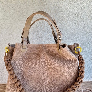Puede incluir: Un bolso tote de cuero marrón tejido con una correa de cuerda trenzada y detalles amarillos.