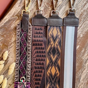 May include: Four adjustable bag straps with metal swivel hooks and dark brown leather attachments. The straps feature varied patterns including geometric diamond designs in black, pink, and tan, a brown textured weave, and a brown striped design.