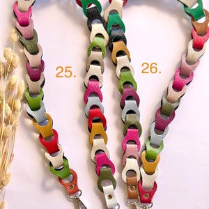 May include: Three colorful, linked leather purse straps. Each strap is made of multiple, interlocking leather pieces in various colors, including green, orange, pink, and white. The straps have silver-colored metal clasps at the ends for attachment.