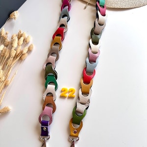 May include: A colorful handbag strap with a chain-link design. The strap is made of leather in various colors, including red, yellow, green, and purple. The strap is approximately 22 inches long and has silver-colored clasps.