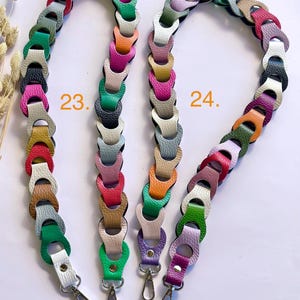May include: Two colorful leather bag straps. One strap is labeled "23." and the other is labeled "24." Each strap is made of linked, multi-colored leather pieces. The straps have silver-colored metal clasps.