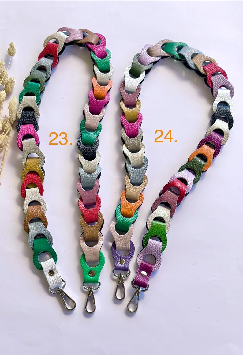 May include: Two colorful leather bag straps. One strap is labeled "23." and the other is labeled "24." Each strap is made of linked, multi-colored leather pieces. The straps have silver-colored metal clasps.
