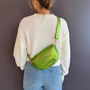 Peut inclure: Un sac banane vert lime métallisé avec une finition lisse et réfléchissante ainsi qu'une sangle réglable assortie. Le sac présente une fermeture éclair dorée sur le bord supérieur et se porte en travers du torse avec un fermoir métallique.