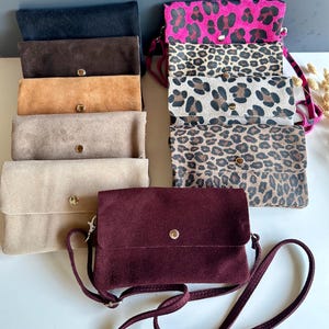 May include: A collection of rectangular suede crossbody bags and clutches in various colours including black, brown, tan, beige, and deep burgundy. Several bags feature leopard print patterns in different scales, and one displays a bright pink leopard print.