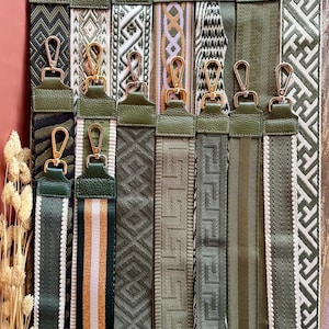 Puede incluir: Una colección de correas de bolso verde oliva y estampadas con cierres dorados. Las correas presentan varios diseños, incluyendo patrones geométricos, a rayas y texturizados. Las correas se muestran sobre un fondo de madera.