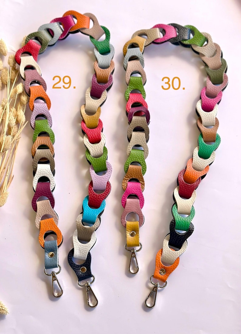 May include: Two colorful purse straps with a chain-link design. Each strap is made of leather in various colors, including pink, green, orange, and blue. The straps have silver-colored metal clasps at the ends for attaching to a purse or bag. The number 29 and 30 are printed on the image.
