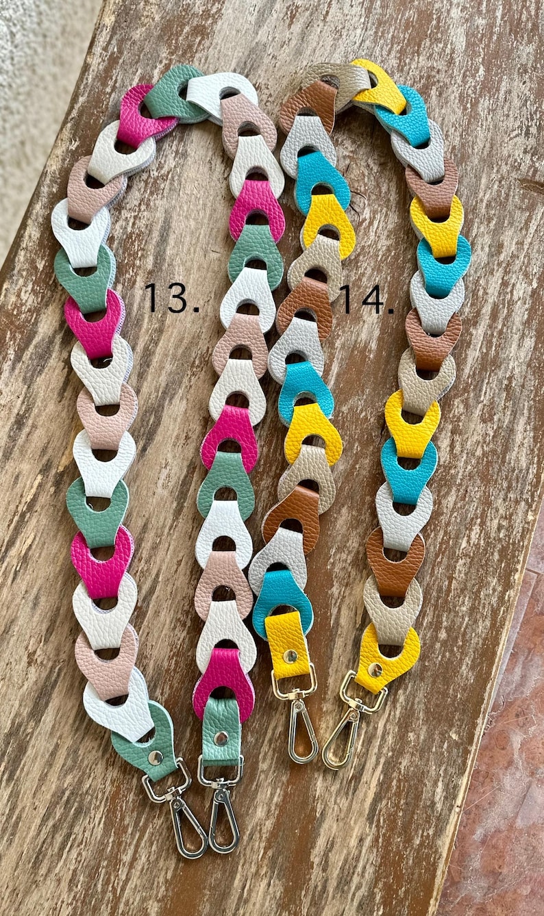 May include: Three colorful purse straps with silver-tone clasps. The straps are made of linked leather pieces in various colors, including pink, green, white, and yellow. The straps are displayed on a wooden surface.