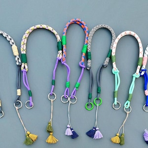 Puede incluir: Siete llaveros de cuerda trenzada de colores con anillos de metal y borlas. Los llaveros son de varios colores, incluyendo azul, verde, morado, rosa y blanco.