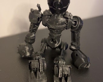 May include: A black, articulated robot figurine with a helmet-like head, round eye, and jointed limbs. The robot has a detailed, mechanical design, with spiked details on the arms and feet. The figurine is posed in a seated position.