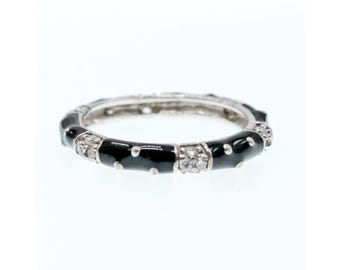 May include: A silver ring with a black enamel band and small white dots. The ring has sections of clear, sparkling stones. The ring is set against a white background.