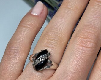 May include: A silver ring with a black oval gemstone and a band decorated with small, sparkling stones.
