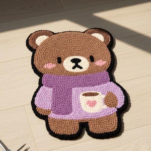 Può includere: Un tappeto a forma di orso marrone con un contorno nero. L'orso indossa un maglione e una sciarpa viola, tenendo in mano una tazza con un cuore rosa. Il tappeto è realizzato in materiale strutturato e poggia su un pavimento in legno chiaro.
