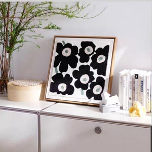 May include: A framed black and white floral artwork with a gold frame. The artwork features a stylized design of black flowers with white centers on a white background.