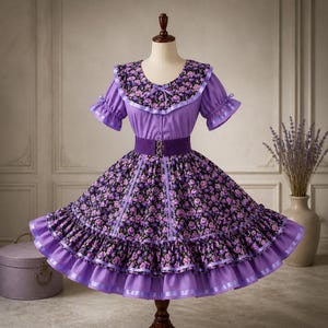 May include: A vintage-style dress in shades of purple and black, displayed on a mannequin. The dress features a floral print skirt, a purple bodice, and a matching collar. A wide purple belt cinches the waist. The dress has short sleeves and is trimmed with ribbons and ruffles.