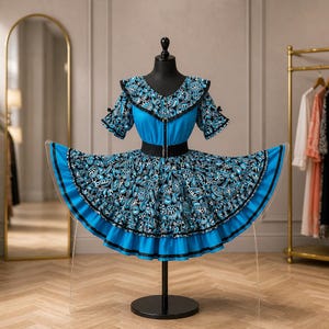 May include: A blue dress with a paisley pattern. The dress has a V-neck, short sleeves, and a black belt. The skirt is flared with black trim. The dress is displayed on a black mannequin. The dress is a vibrant piece.
