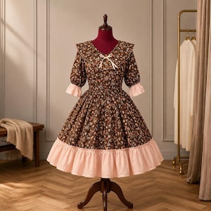 Puede incluir: Vestido marrón con estampado floral, con dobladillo y mangas con volantes, exhibido en un maniquí. El vestido presenta un volante rosa en contraste en el dobladillo y los puños, y un lazo blanco en el escote. El vestido tiene una estética vintage.