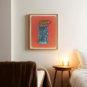 Art print of a water bottle that has the works "drink your water" on it in blue. The water bottle lid is green and the background is salmon pink.