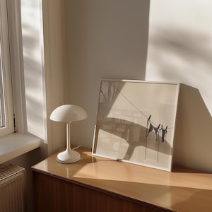Horizontal art print of a bikini set hanging on a clothesline. The bathing suit is dark grey and in the bottom right of the artwork. The background is tan/beige.