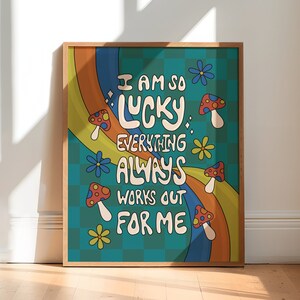 May include: A framed art print with a retro design. The artwork features the text "I AM SO LUCKY EVERYTHING ALWAYS WORKS OUT FOR ME" in white, along with colorful mushrooms, flowers, and a rainbow. The background is teal with a checkered pattern.