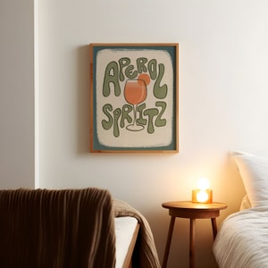 Art Print of an aperol spritz with an orange wedge on the glass. The words "aperol spritz" surround the drink in green. A tan hand drawn rectangle is behind it and the background is a solid color dark teal.