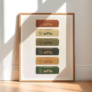 Op de afbeelding: Een ingelijst afdruk van een stapel van zes boterstokken in verschillende kleuren, elk met de tekst "NET WT 4 OZ (113g) SALTED BUTTER" gedrukt op het etiket.
