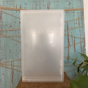 May include: A rectangular, semi-transparent, frosted plastic storage case with a hinged lid. The container features a smooth, matte finish and a simple, functional design, providing a clear view of the contents stored inside the protective shell.