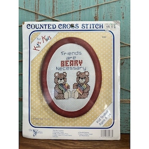 May include: A counted cross stitch kit for kids featuring two brown teddy bears holding flowers and the text "Friends are Beary Necessary". The kit includes a Victorian frame, DMC embroidery floss, 11-count fabric, needle, fiberfill batting, and an easy-to-follow graph and illustrations. The finished size is 5 inches by 6 inches.