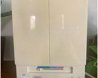 May include: A cream-colored Jerdon lighted makeup mirror with two folding doors. The base features a sliding light setting switch labeled Day, Office, Evening, and Home, a power outlet, and an on-off rocker switch on the front panel.