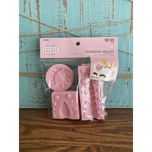 Puede incluir: Un juego de cuatro moldes de fondant rosa para hacer decoraciones de pastel de unicornio. Los moldes están empaquetados en una bolsa de plástico transparente con una etiqueta rosa y blanca que dice "Sunny Side Up Bakery" y "Moldes de fondant 1.45-3.78in (3.68-9.60cm)".