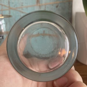 Puede incluir: Un vaso transparente con un borde gris, visto desde abajo. El vaso tiene una base redondeada y una superficie ligeramente texturizada. El borde es de color gris s&oacute;lido y el vaso parece estar limpio.
