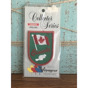 May include: A green and red embroidered patch with the Canadian flag and the word "Canada" in red lettering. The patch is on a white card with the text "Collector Series" and "Canada Emblems".