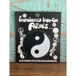 May include: Black and white embroidered iron-on patch of a yin yang symbol. The patch is on a black card with the text "Embroidered Iron-On Patches by Kalan" and "Cool for jeans, tops, jackets, hats, backpacks, etc."