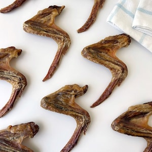 K&ouml;nnte beinhalten: Nahaufnahme von neun getrockneten H&auml;hnchenfl&uuml;geln auf einer wei&szlig;en Oberfl&auml;che. Die Fl&uuml;gel sind braun und haben eine leicht knusprige Textur.