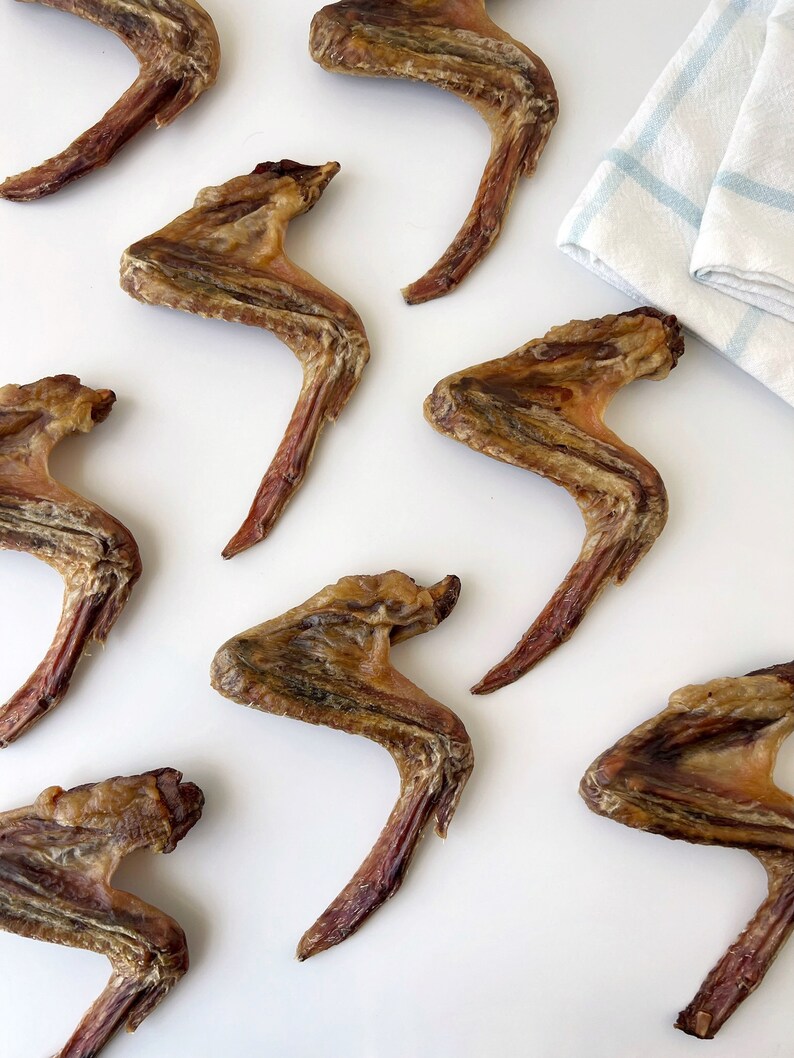 K&ouml;nnte beinhalten: Nahaufnahme von neun getrockneten H&auml;hnchenfl&uuml;geln auf einer wei&szlig;en Oberfl&auml;che. Die Fl&uuml;gel sind braun und haben eine leicht knusprige Textur.