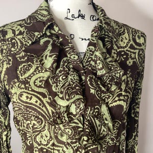 Może przedstawiać: Brązowa bluzka z długimi rękawami w wzór paisley w kolorze zielonym, z falbaniastym kołnierzem.