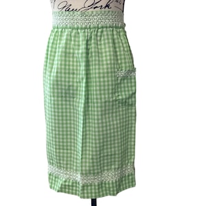 Puede incluir: Delantal de cuadros vichy verde y blanco con ribete de encaje blanco y un solo bolsillo.