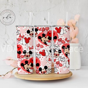 May include: Three stainless steel tumblers with a Valentine's Day theme. The design features Mickey and Minnie Mouse, red hearts, and heart-shaped balloons. The tumblers have a white background with a repeating pattern and clear straws.