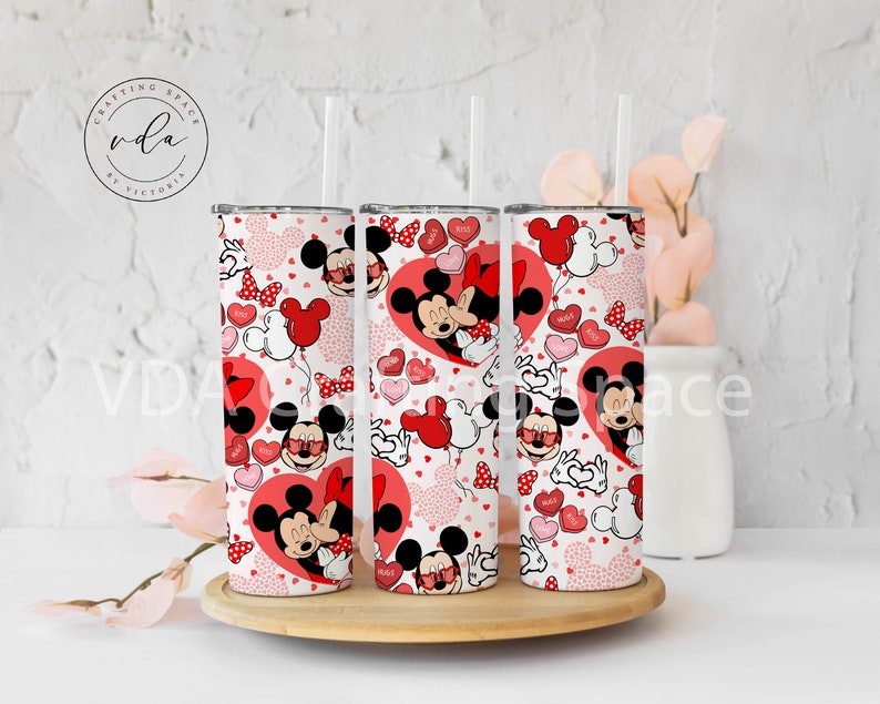 May include: Three stainless steel tumblers with a Valentine's Day theme. The design features Mickey and Minnie Mouse, red hearts, and heart-shaped balloons. The tumblers have a white background with a repeating pattern and clear straws.