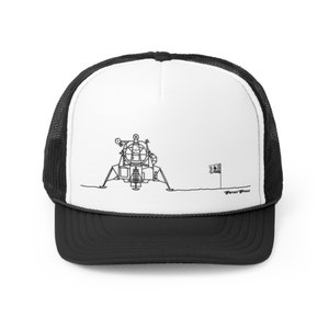 Op de afbeelding: Een zwart-witte illustratie van de maanlander op de maan met een vlag die in het oppervlak is geplant. De afbeelding is gedrukt op een witte trucker-pet met een zwart mesh-achterkant.