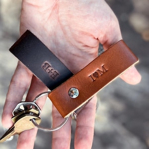 May include: Two leather keychains, one dark brown and one light brown, held together by a silver keyring. The dark brown keychain has the initials "B+B" embossed, while the light brown keychain has "I♡M".