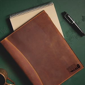 Pu&ograve; includere: Una copertina per quaderno in pelle marrone con dettagli di cuciture gialle. La copertina ha il testo "YOUR BLOG" stampato in nero nell'angolo in basso a destra.