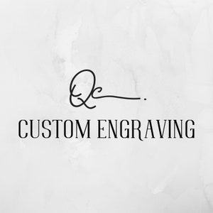 May include: A black and white logo with a stylized signature and the text "CUSTOM ENGRAVING".