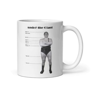 Könnte beinhalten: Weiße Keramiktasse mit einem Schwarzweißbild von André the Giant, einem Wrestler, der neben einer Höhentabelle steht. Der Text "André the Giant" ist oben auf der Tasse in Schwarz gedruckt.