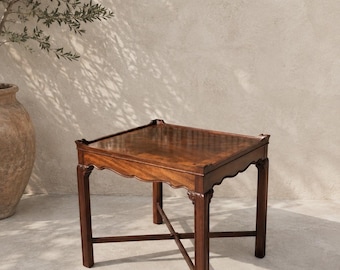 May include: A square wooden side table with a dark brown finish, featuring a flat top with raised edges, a scalloped apron design along the sides, four straight legs, and a cross-shaped stretcher connecting the legs near the base.