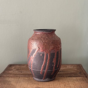 May include: A black ceramic vase with a copper glaze dripping down the sides. The vase has a textured surface and a rounded shape.
