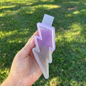 May include: A clear resin lightning bolt charm with a purple and white glitter fill.