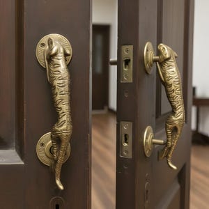 Può includere: Maniglie per porte in ottone dorato ornate con un design a tigre. Le maniglie sono montate su una porta in legno marrone scuro. La porta è leggermente socchiusa, rivelando uno scorcio dell'interno.