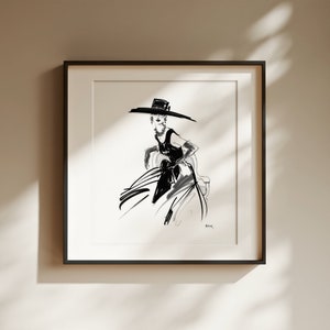 Pu&ograve; includere: Illustrazione a inchiostro nero e bianco di una persona con un cappello a tesa larga e un vestito. L'opera &egrave; incorniciata in una cornice quadrata nera e montata su una parete di colore neutro. Lo stile ricorda un bozzetto di moda.